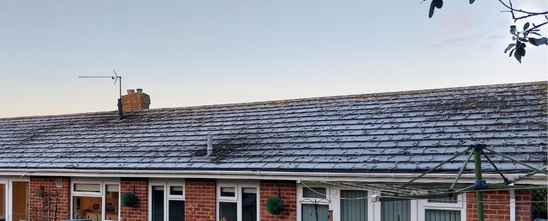 A bungalow roof dark with moss and lichen, before cleaning
